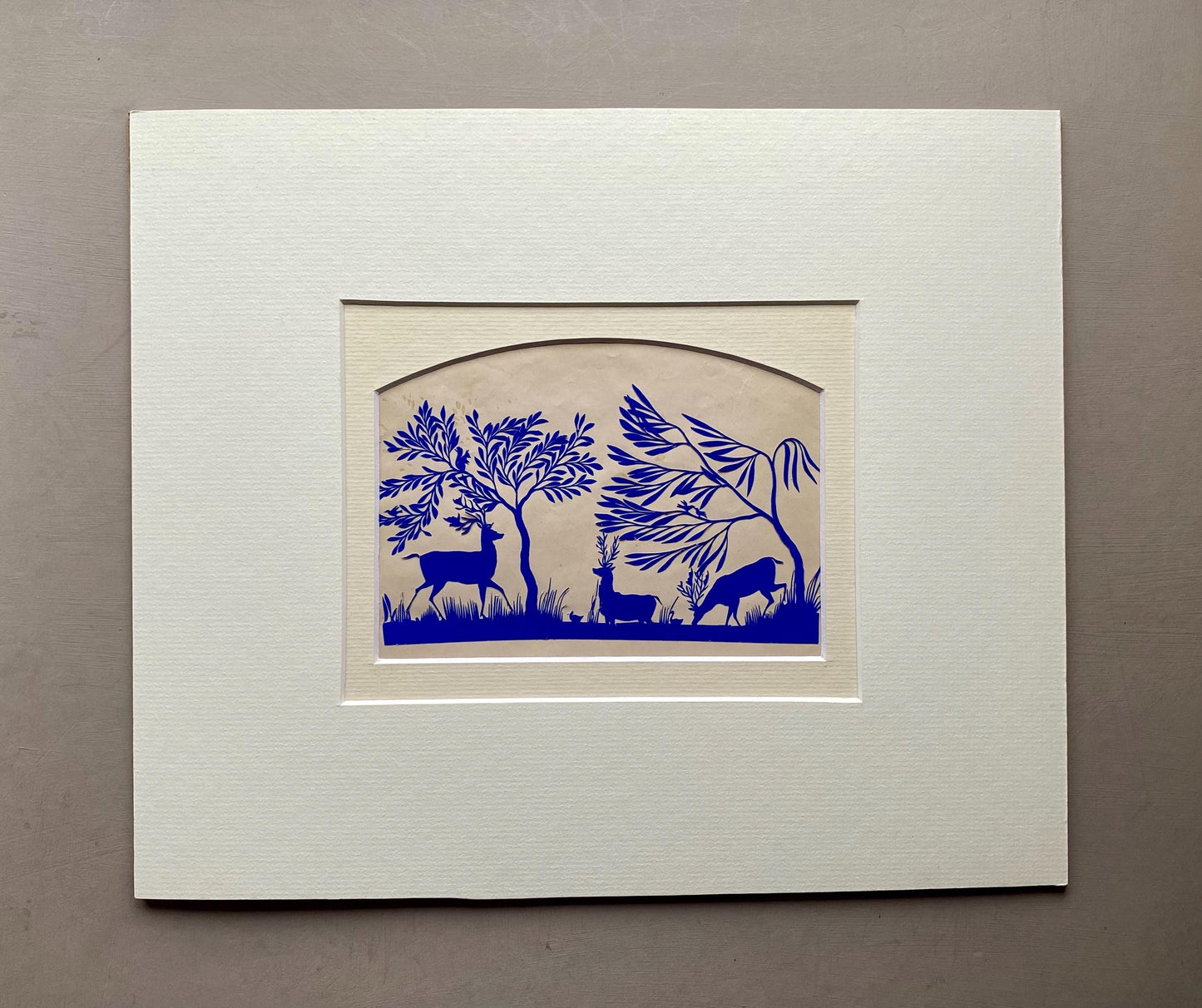 An Antique Paper Cut. Deer At A Pond. Blue on a Pinkish Cream Ground. Late Georgian, Early Victorian. Size: 12.7 x 21.5 cms.