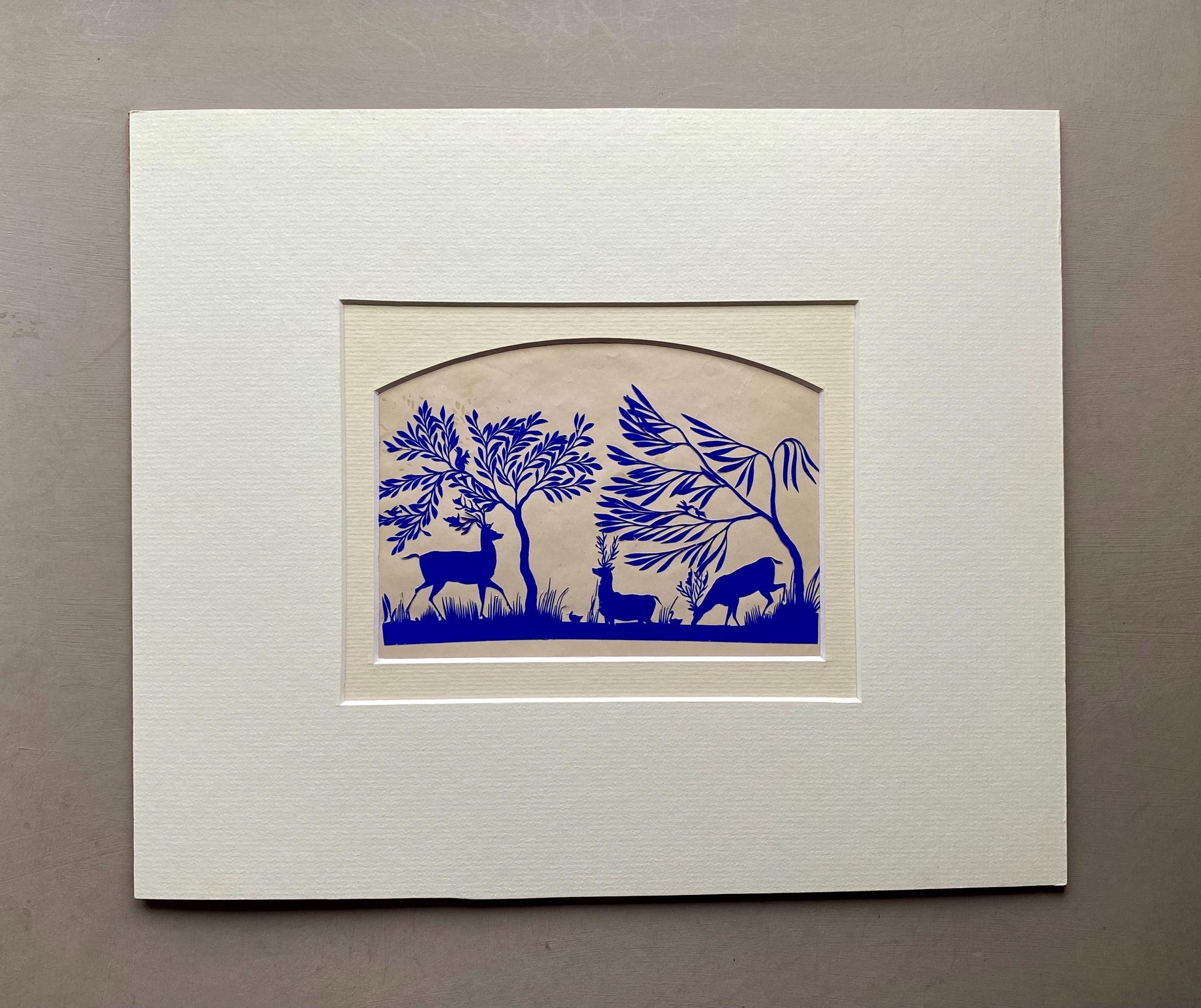 An Antique Paper Cut. Deer At A Pond. Blue on a Pinkish Cream Ground. Late Georgian, Early Victorian. Size: 12.7 x 21.5 cms.