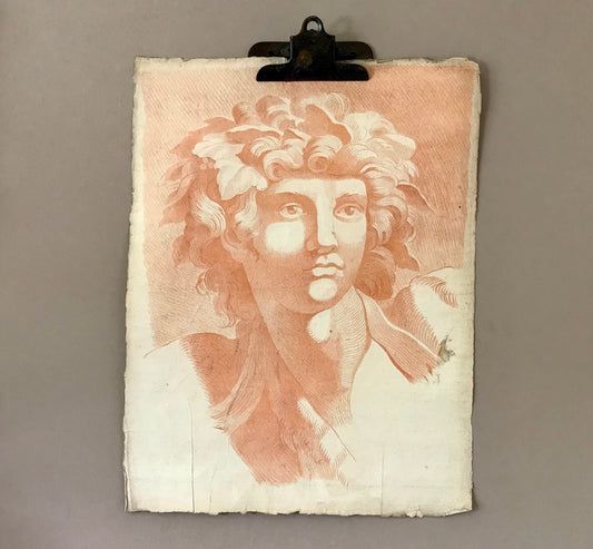 May include: A vintage print of a classical bust, rendered in shades of peach and white. The artwork, held by a metal clip, depicts a figure with curly hair and a serene expression. The paper has a textured, aged appearance, suggesting its antique nature.