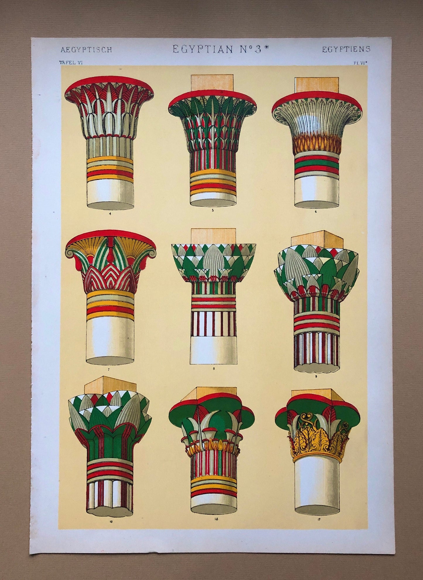May include: A vintage illustration of nine different Egyptian column capitals. The capitals are painted in various colors, including red, green, yellow, and white. The illustration is titled "Egyptian No. 3*" and is from a book titled "Aegyptisch Tafel VI".