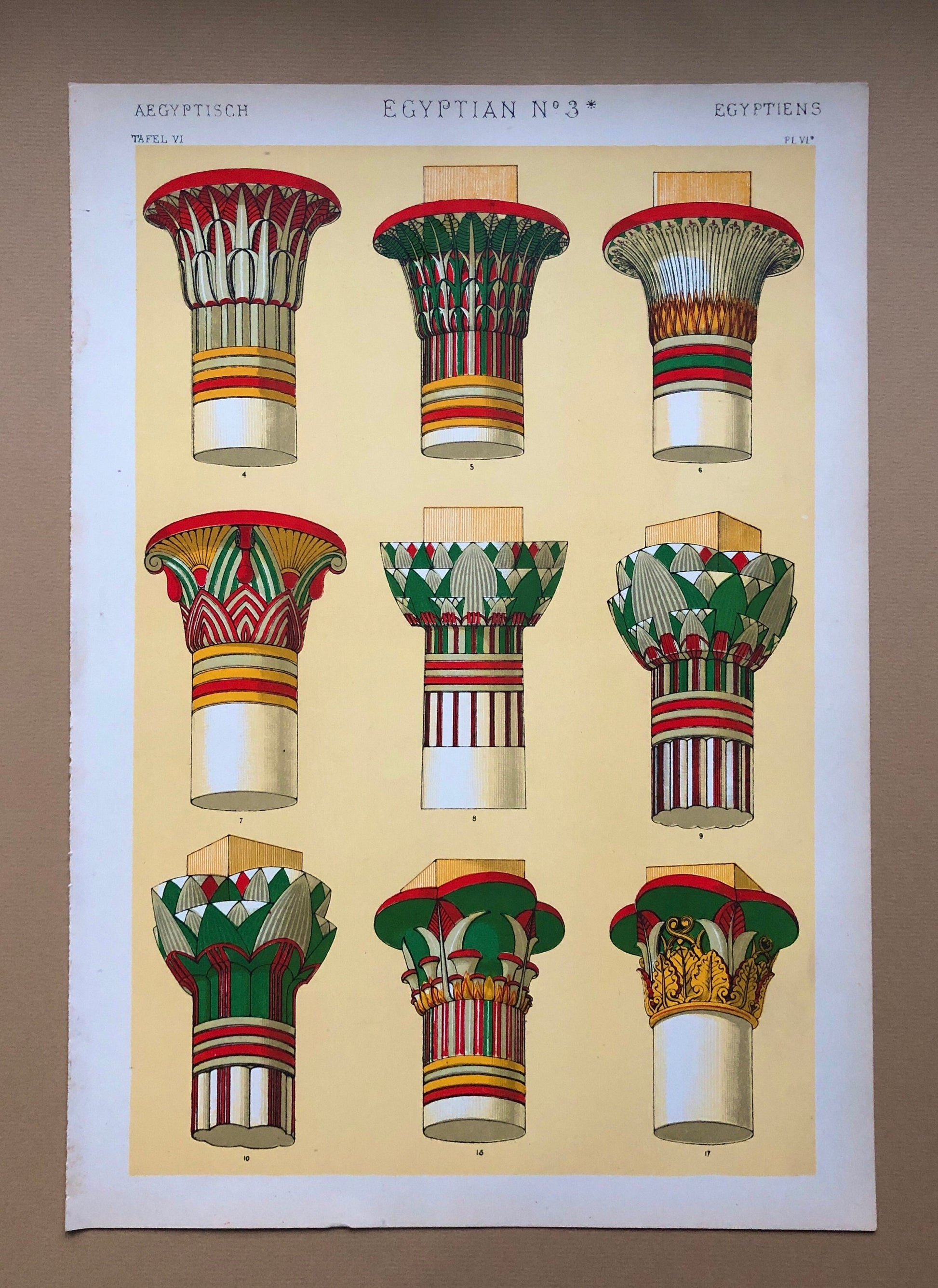 May include: A vintage illustration of nine different Egyptian column capitals. The capitals are painted in various colors, including red, green, yellow, and white. The illustration is titled "Egyptian No. 3*" and is from a book titled "Aegyptisch Tafel VI".