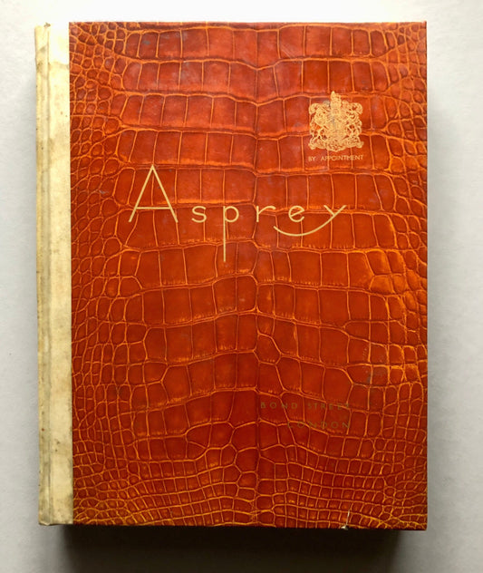 May include: A brown leather-bound book with the word "Asprey" embossed in gold lettering on the front cover. The book also features a gold crest with the text "By Appointment" underneath.