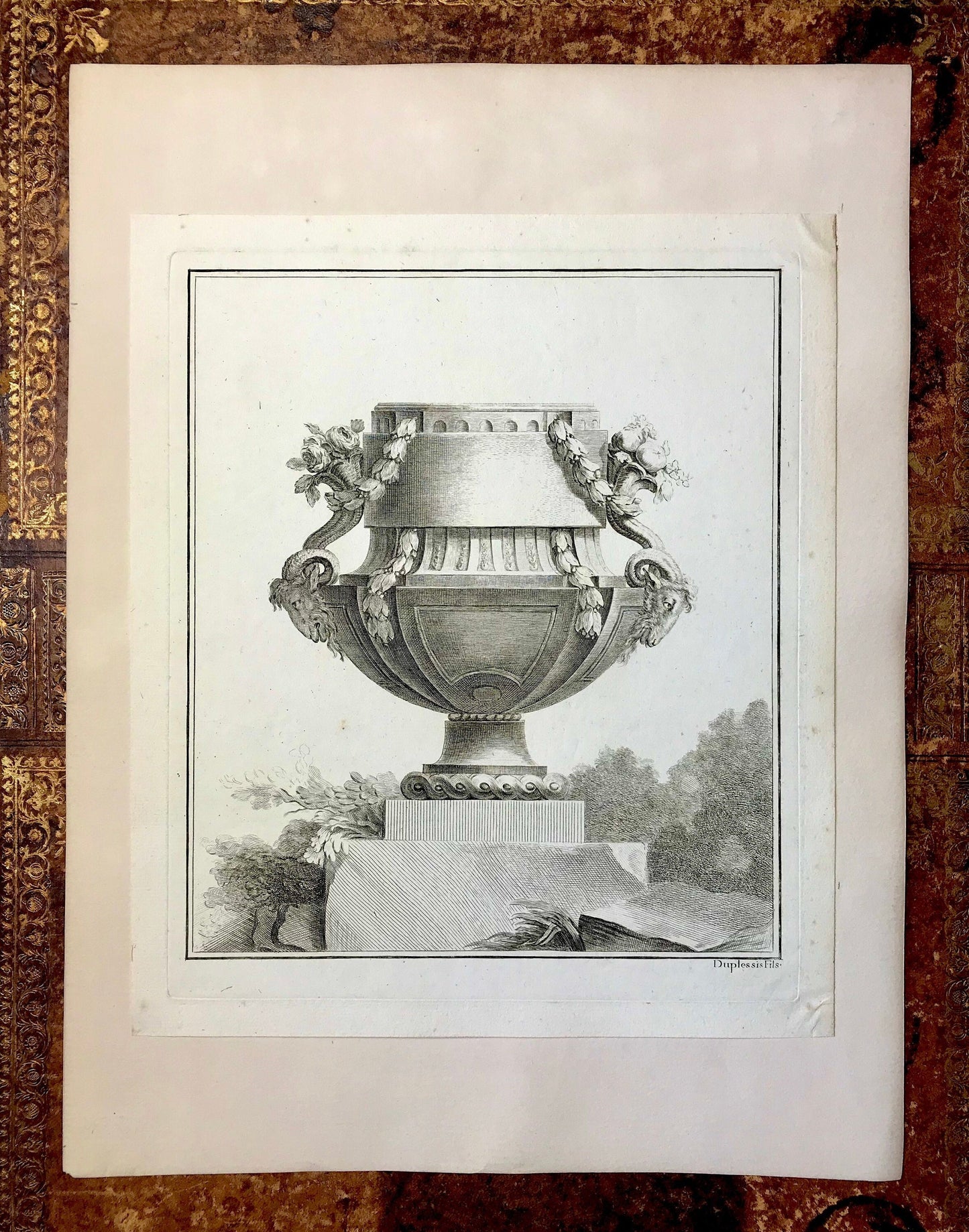 May include: A black and white engraving of a decorative urn with floral accents. The urn is on a pedestal and surrounded by foliage. The engraving is signed "Duplessis".