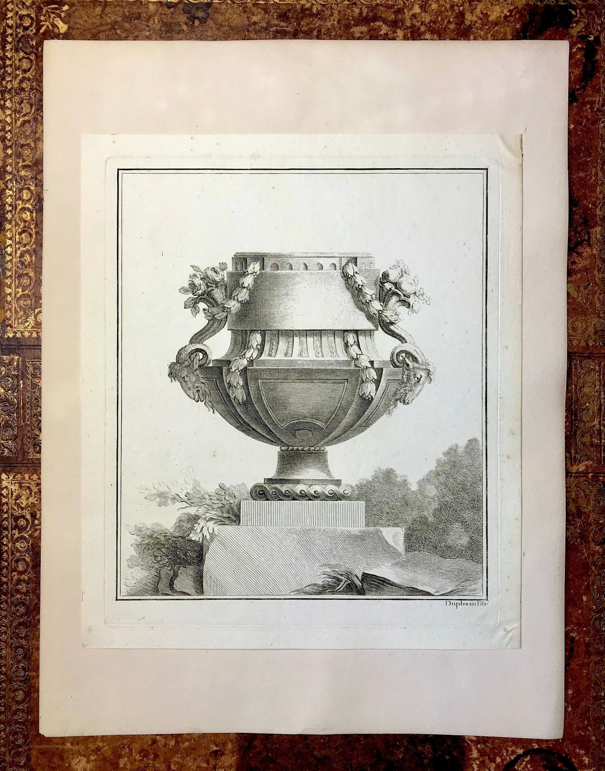 May include: A black and white engraving of a decorative urn with floral accents. The urn is on a pedestal and surrounded by foliage. The engraving is signed "Duplessis".
